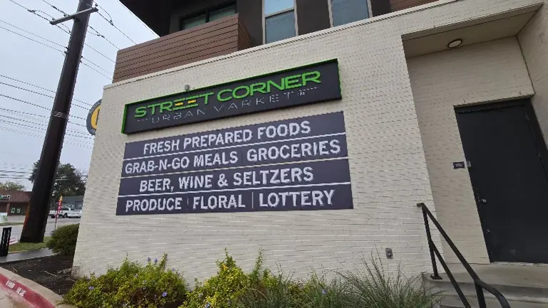 : The exterior of the store, prominently featuring signage that communicates a wide range of fresh and prepared foods, alongside other essential offerings like