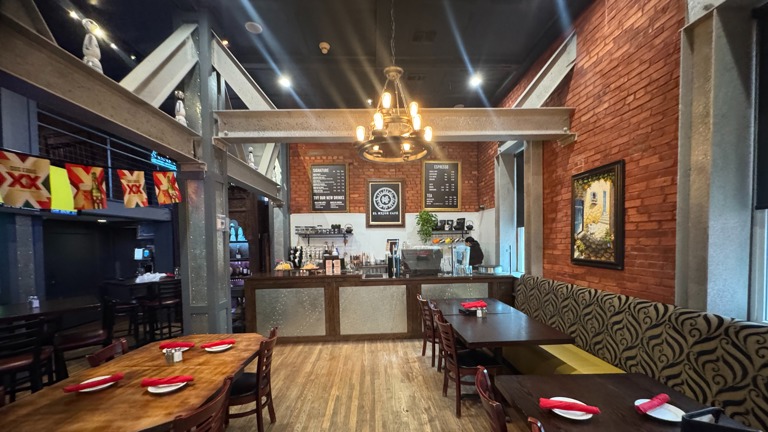 Coffee space with a chandelier, wood finished floors, brick wall, and a towering ceiling