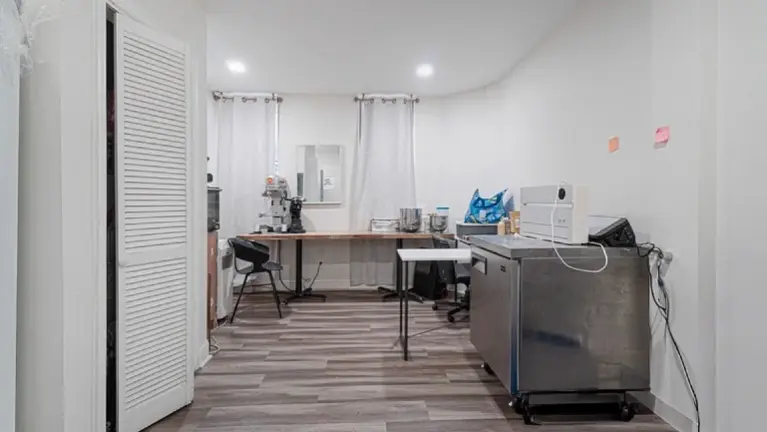 Back office / workspace area with wood-look flooring. Long wooden counter with a large commercial mixer, a stainless steel rolling cabinet. Closet.