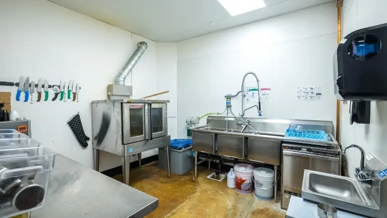 Back-of-house kitchen and prep area with commercial oven, multi-bay stainless sinks, and ample workspace — ready for food service operation. Back-of-house kitchen and prep area with commercial oven, multi-bay stainless sinks, and ample workspace — ready for food service operation.