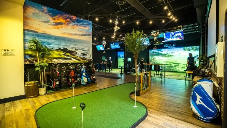 Indoor putting green with bag drop area and mural backdrop — a versatile space for short-game practice, lessons, and casual play. Indoor putting green with bag drop area and mural backdrop — a versatile space for short-game practice, lessons, and casual play.