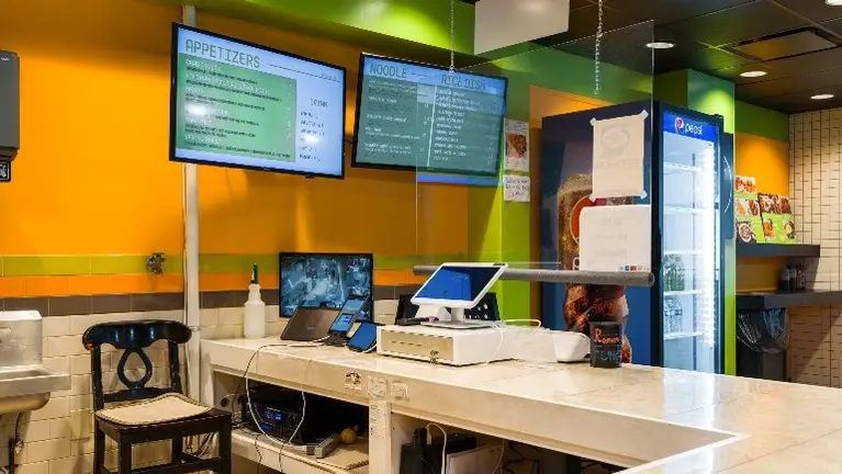 Front counter area with POS system, digital menu boards, drink cooler, and service setup. Front counter area with POS system, digital menu boards, drink cooler, and service setup.