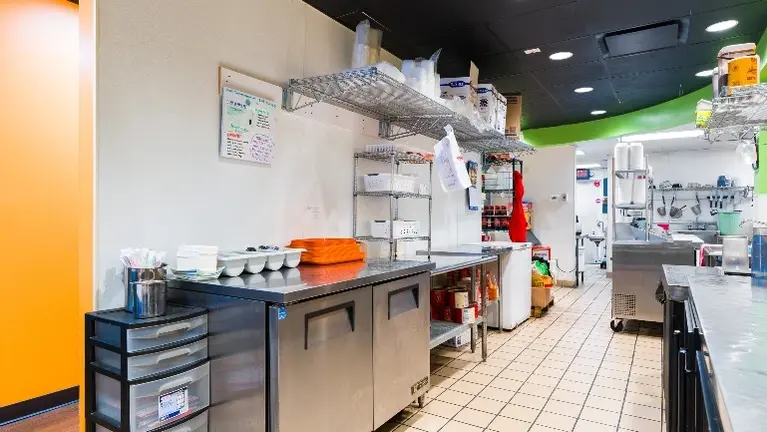 Prep and service area with stainless equipment, storage shelving, coolers, and kitchen access. Prep and service area with stainless equipment, storage shelving, coolers, and kitchen access.