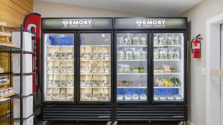 Dual commercial display coolers branded with the Emory Market Gardens logo — fully stocked with packaged gourmet mushrooms and garden-fresh seasonal produce, a