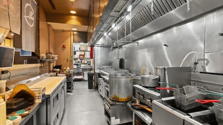 Cook line under stainless exhaust hood with wok range, flat-top griddle, and open burners.