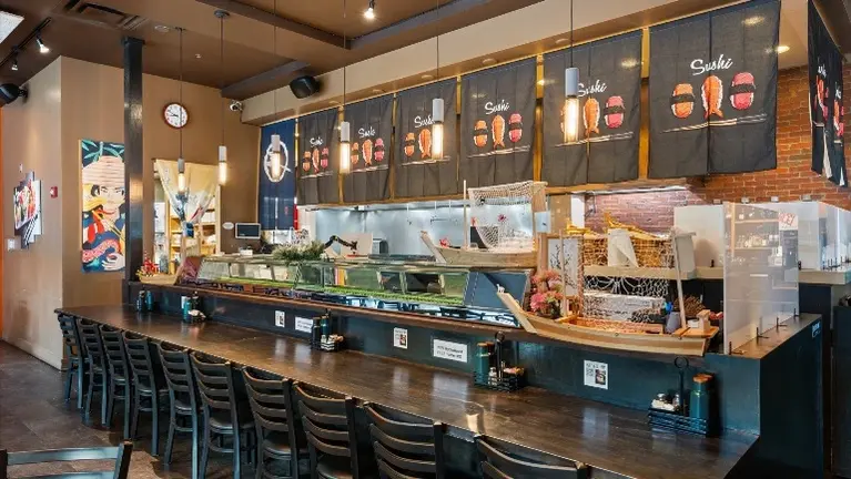 Sushi counter with refrigerated display case, stainless prep surface, and counter seating.