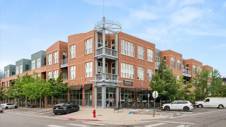 Building exterior at the street corner, brick and metal panel construction with ground-floor storefront.